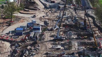 Active construction site with cranes lifting materials, workers in motion, bridge supports, excavation areas, and nearby roads and greenery. video