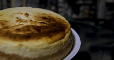 Closeup of a steel cake serving tool carefully lifting up and pulling out the first triangular slice of a whole round, soft, baked cheesecake dessert on a plate. video