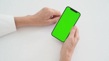 Female Hands Holding Smartphone with Green Screen Chromakey on White Table, Tapping Display, Navigating Mobile Interface, Digital Device Interaction, Online Communication, App UI Customization video