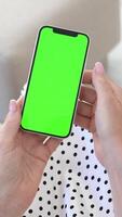 mulher sentado em sofá segurando Smartphone com verde tela, usando toque tela, noivando com digital dispositivo, sem fio comunicação, moderno tecnologia, casa conforto, croma chave para personalizadas conteúdo video