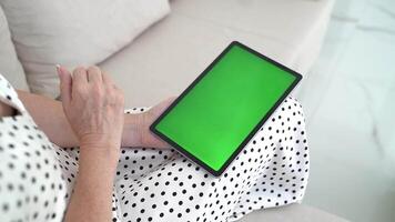 Tablet with Green Chromakey Screen in Hands of Woman Sitting on Sofa, Browsing, Scrolling, Touching Display, Digital Interaction, Cozy Modern Interior, Bright Comfortable Space video