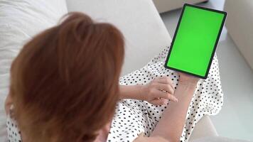 Hands from above grasp tablet with vibrant green display, interacting with dynamic content in cozy home environment. Digital mockup highlights chroma key technology for seamless screen replacement video