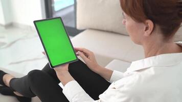Redhead Woman Sitting on Sofa in White Shirt Using Tablet with Green Screen, Navigation Display, Exploring Digital Content, Wireless Communication, Modern Technology in Bright Living Room video