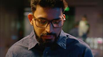 Indian man in glasses ethnic businessman business guy programmer trader wear eyeglasses reflection computer screen trading coding male eyes eyesight looking at camera professional hacker broker office video