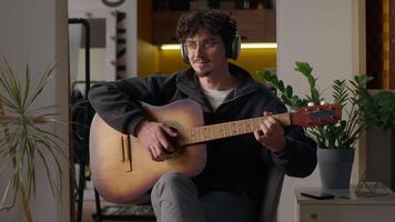 Smiling Caucasian musician guy playing guitar solo at home hipster man in headphones male hobby relaxing music performance song happy artist enjoying play acoustic musical instrument practicing skills video