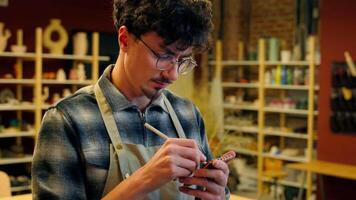 Pensive man writing notes in pottery workshop male Caucasian guy smiling glad art designer small business owner artist potter craftsman write list tasks artwork draw sketch in studio creative handmade video