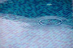 Rippling patterns form on the tranquil surface of a blue-tiled pool on a sunny afternoon photo