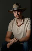 Portrait of a young man in a straw hat seated in dim lighting, reflecting thoughtful contemplation in a stylish setting photo