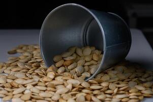 Pumpkin seeds spilling from a silver bucket create a rustic autumn aesthetic on a wooden surface photo