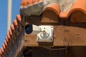 Surveillance camera monitoring a rustic building under clear blue skies in a sunny environment photo