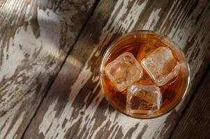 Refreshing drink with ice cubes resting on rustic wooden surface during golden photo