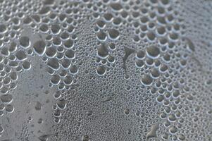 Water droplets collect on a glass surface reflecting intricate patterns under soft light photo