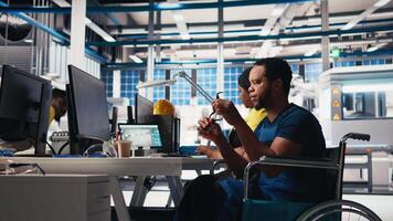 African american wheelchair user working in solar panel factory, optimizing systems for renewable energy. Engineer examines robot arms automation in a disability friendly power plant. Camera B. video