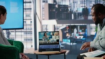 Multiethnic business leaders engaged in a web conference in office lobby, exchanging strategy and negotiation points with remote partners in a global multicultural work environment. Camera B. video