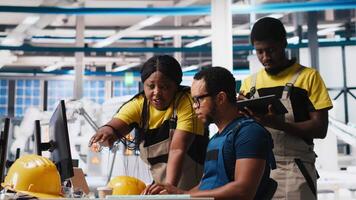 Photovoltaics factory team reviews solar panels manual production, monitoring the performance on computer program. Group of black employees reads plant machinery parameters. Camera A. video