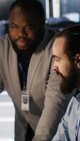 Vertical Server farm manager overseeing engineer examining neural network algorithms. Data center team leader and worker reviewing performance dashboards of artificial intelligence infrastructure, camera A video