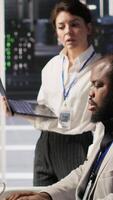 Vertical Happy data center manager providing positive feedback to engineer developing neural networks software on computer. Cheerful supervisor pleased by employee work implementing AI in server room, camera A video