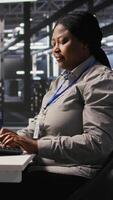 Vertical Woman in data center doing software updates, verifying machine learning parameters. Server farm IT expert using PC to inspect configurations, ensuring optimal application performance, camera A video