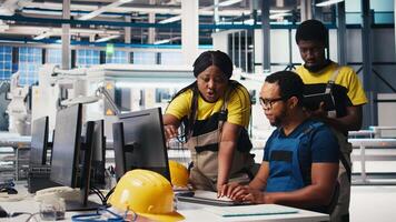 Photovoltaics factory team reviews solar panels manual production, monitoring the performance on computer program. Group of black employees reads plant machinery parameters. Camera B. video
