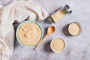 Sesame tahini in a bowl and sesame seeds in a bowl on the table top view photo