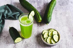 A glass of fresh cucumber juice and cucumbers on the table photo