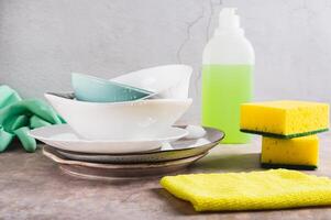 Stack of plates in foam, cloth, sponges, gloves and detergent on table photo