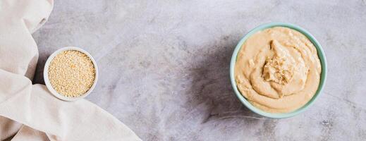 Homemade sesame tahini in bowl on grey table top view web banner photo
