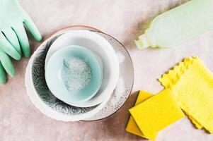Stack of plates in foam, cloth, sponges, gloves and detergent on table top view photo