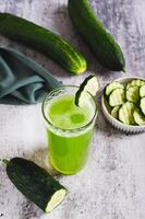 A glass of fresh cucumber juice and cucumbers on the table vertical view photo
