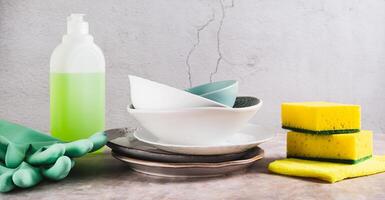 Stack of plates in foam, cloth, sponges, gloves and detergent on table web banner photo