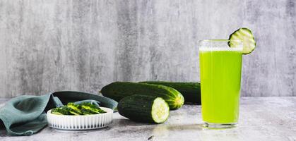 Fresh cucumber juice in a glass and cucumber pieces in a bowl on the table web banner photo