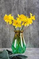 Fresh spring flowers yellow daffodils in vase on grey table vertical view photo