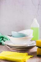 Stack of plates in foam, cloth, sponges, gloves and detergent on table vertical view photo