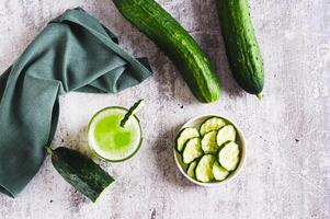 Fresh cucumber juice in a glass and cucumber pieces in a bowl on the table top view photo