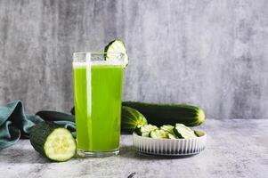 Fresh cucumber juice in a glass and cucumber pieces in a bowl on the table photo