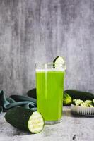 Fresh cucumber juice in a glass and cucumber pieces in a bowl on the table vertical view photo