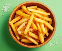 Top down view of a bowl fill with long crispy fries seasoned with visible grains of salt photo