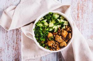 Close up of buckwheat porridge with meat, cucumber and chives in a bowl on the table top view photo