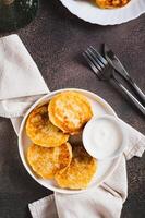 Appetizing potato fritters and sour cream on a plate on the table top and vertical view photo