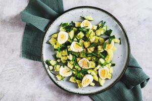 Close up of fresh salad of cucumbers, quail eggs and green onions on a plate top view photo