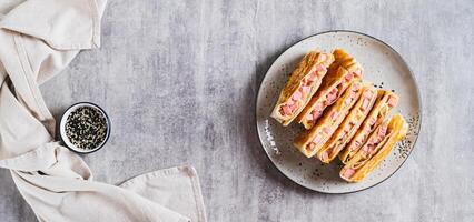 Crispy envelopes with sausage and cheese in flat bread on a plate top view web banner photo