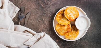 Appetizing potato fritters and sour cream on a plate on the table top view web banner photo