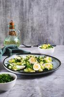 Fresh salad of cucumbers, quail eggs and green onions on a plate on the table vertical view photo