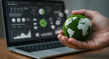 Green Earth in Hand Near Laptop with Environmental Data photo