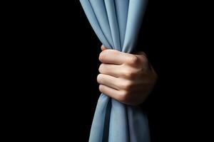Hand grasps blue curtain against black backdrop, creating sense of anticipation and unveiling. Dramatic concept photo