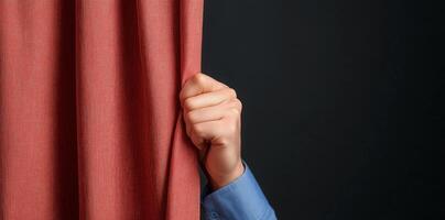Hand pulls back red curtain, revealing sense of mystery and anticipation against dark background, embodying drama of theater performance. Stage concept photo