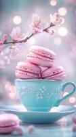 Pink macarons in teal teacup with delicate spring blossoms, against soft bokeh background, creating sweet springtime treat. Food concept photo