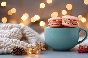 Pink macarons in teal mug with cozy knitted blanket, pine cone, and festive lights, creating sweet and warm Christmas treat scene. Holiday concept photo