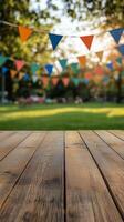 Vertical image of rustic wooden table with blurred background of colorful bunting strung between trees in sunny park for showcasing products and summery designs. Celebration concept photo