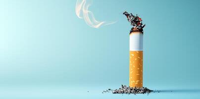Single burning cigarette with ash and smoke against minimalist blue background. Smoking cessation concept photo